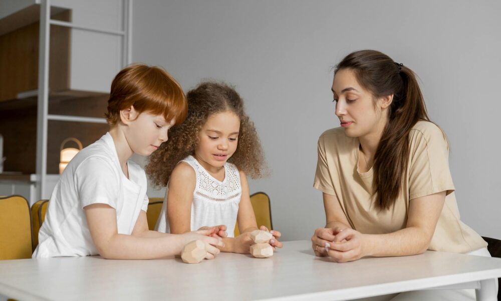 woman sitting beside two kids stacking a pile of stones on a white table